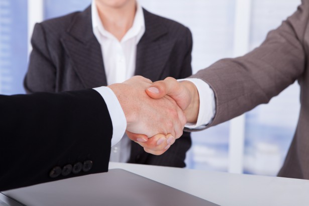 Cropped image of businessmen shaking hands in front of female colleague at office